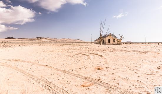 surreale Wüstenlandschaft mit Bahnlinie und einsamem Haus 